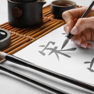Ein Mensch schreibt mit einer Feder asiatische Schriftzeichen auf ein Papier. 